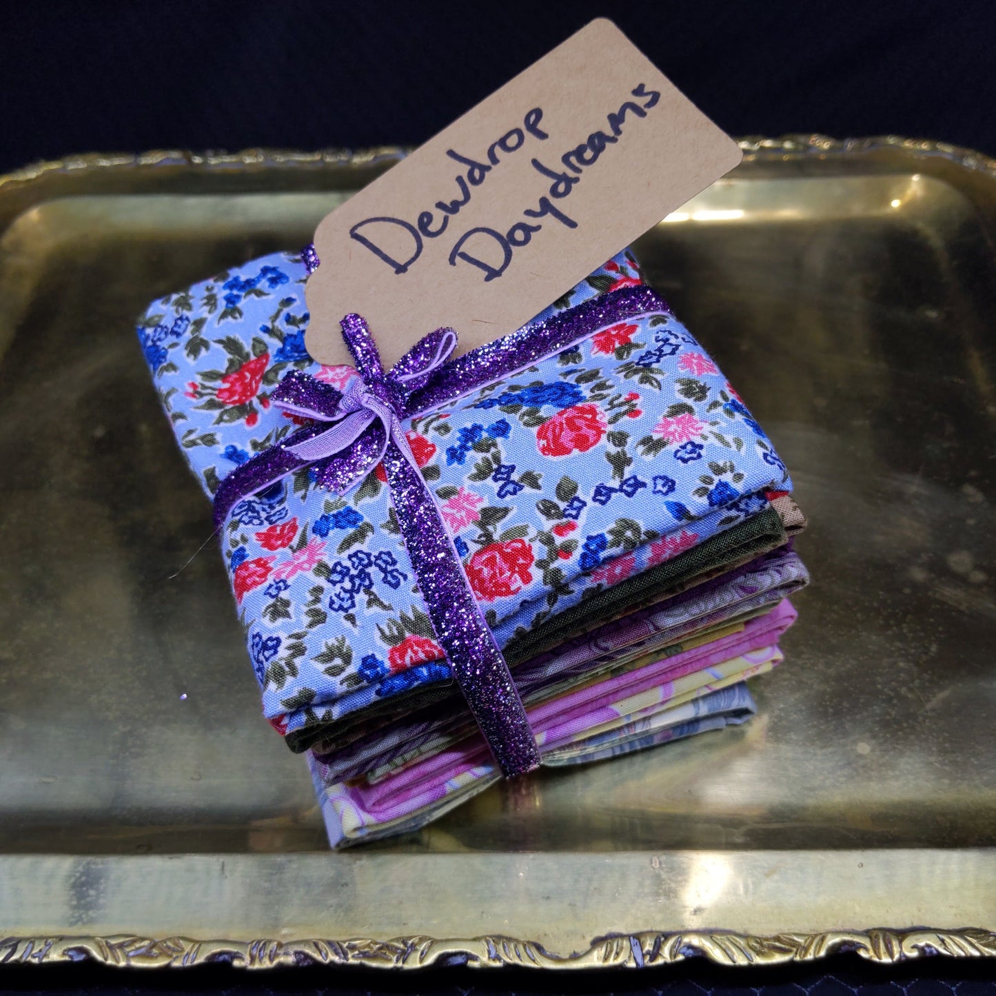 Floral fabric pouches with a purple ribbon on a metallic surface, accompanied by a 'Dewdrop Daydreams' tag.