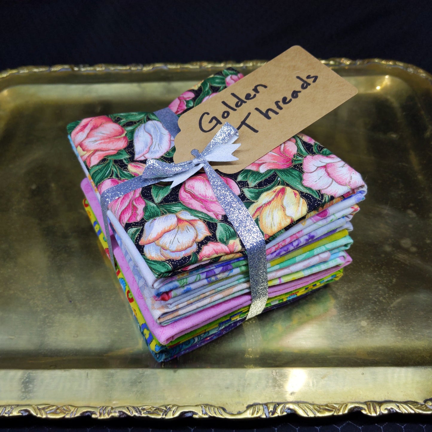 Stack of colorful fabric squares with a floral pattern on a gold tray.